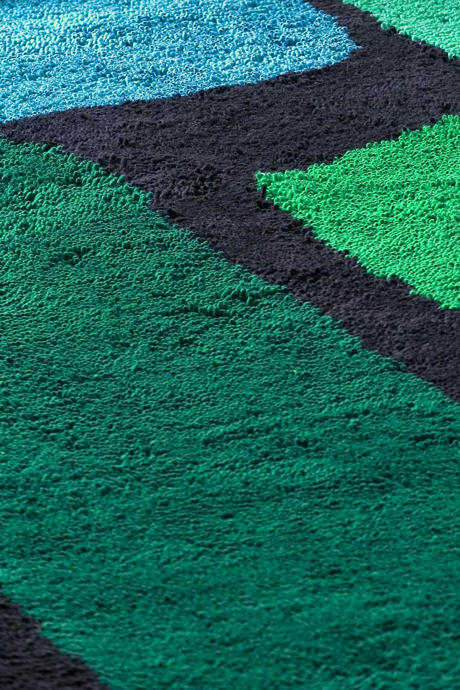 close up of jewel rug by dinosaur designs green and blue large shapes on black background